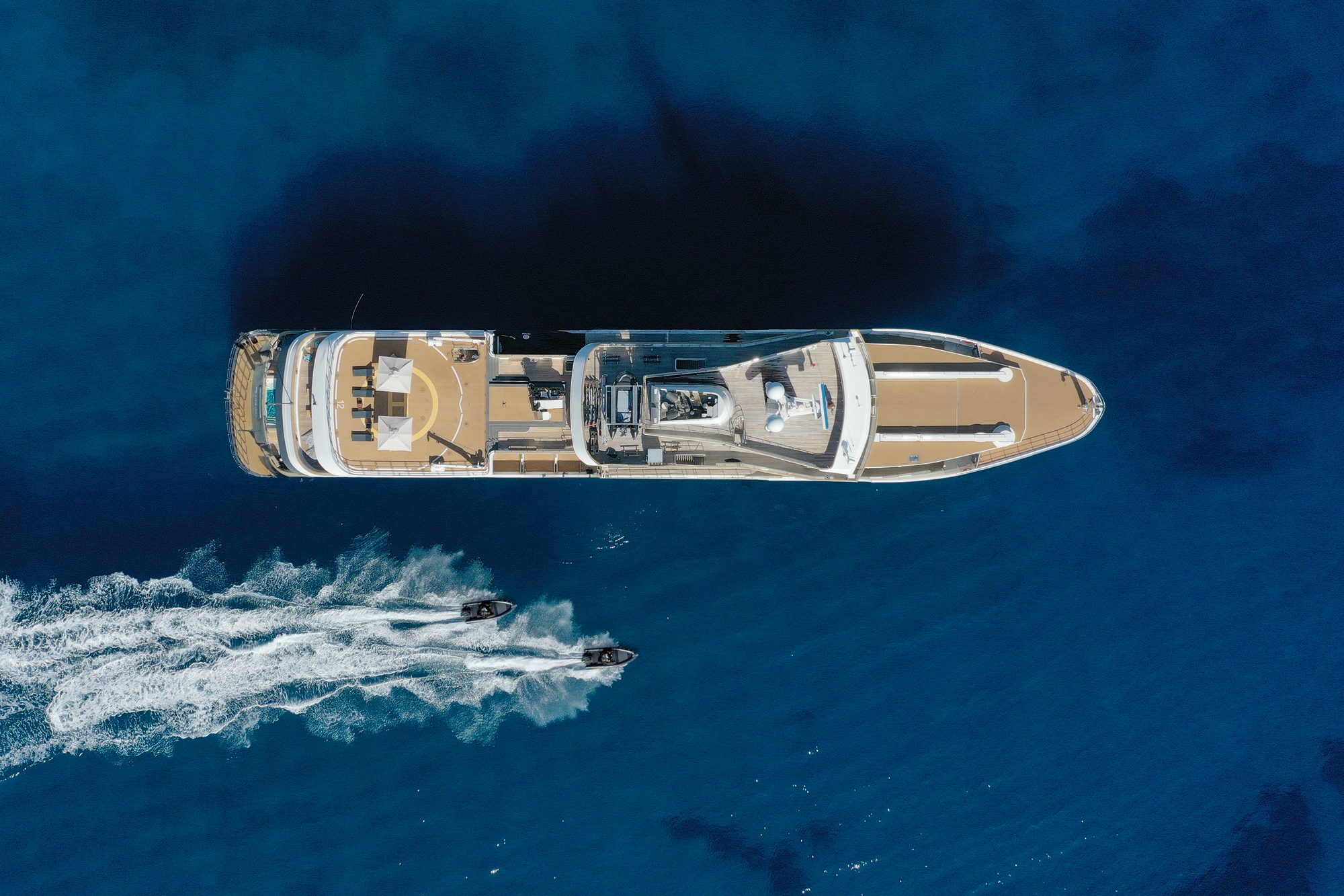 Aqua Lares from directly above in deep blue water, two tenders leaving white wakes alongside
