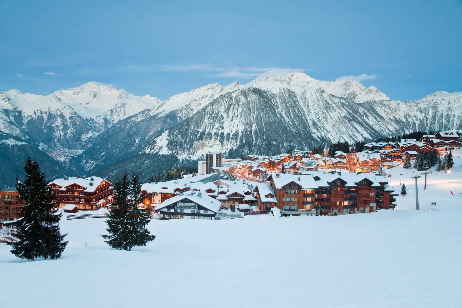 Courchevel 1850 at dusk, hotels and chalets lit beneath the mountains