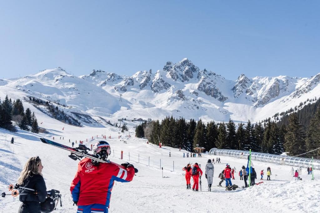 A ski instructor carrying skis towards a beginners' slope below the peaks